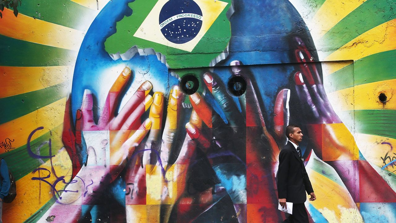 SAO PAULO, BRAZIL - JUNE 10: A man passes graffiti of multi-colored hands supporting the planet marked with a Brazilian flag on June 10, 2014 in Sao Paulo, Brazil. The opening match for the 2014 FIFA World Cup is June 12 in Sao Paulo when Brazil takes on Croatia. (Photo by Mario Tama/Getty Images)