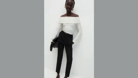 M&S M&S model poses in white top and black trousers and leans against a white wall