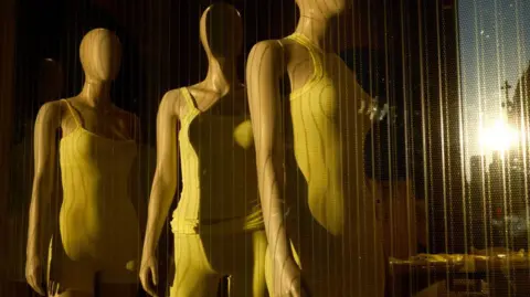 Getty Images Three mannequins displaying Skims' shapewear behind a window at a pop-up shop in New York