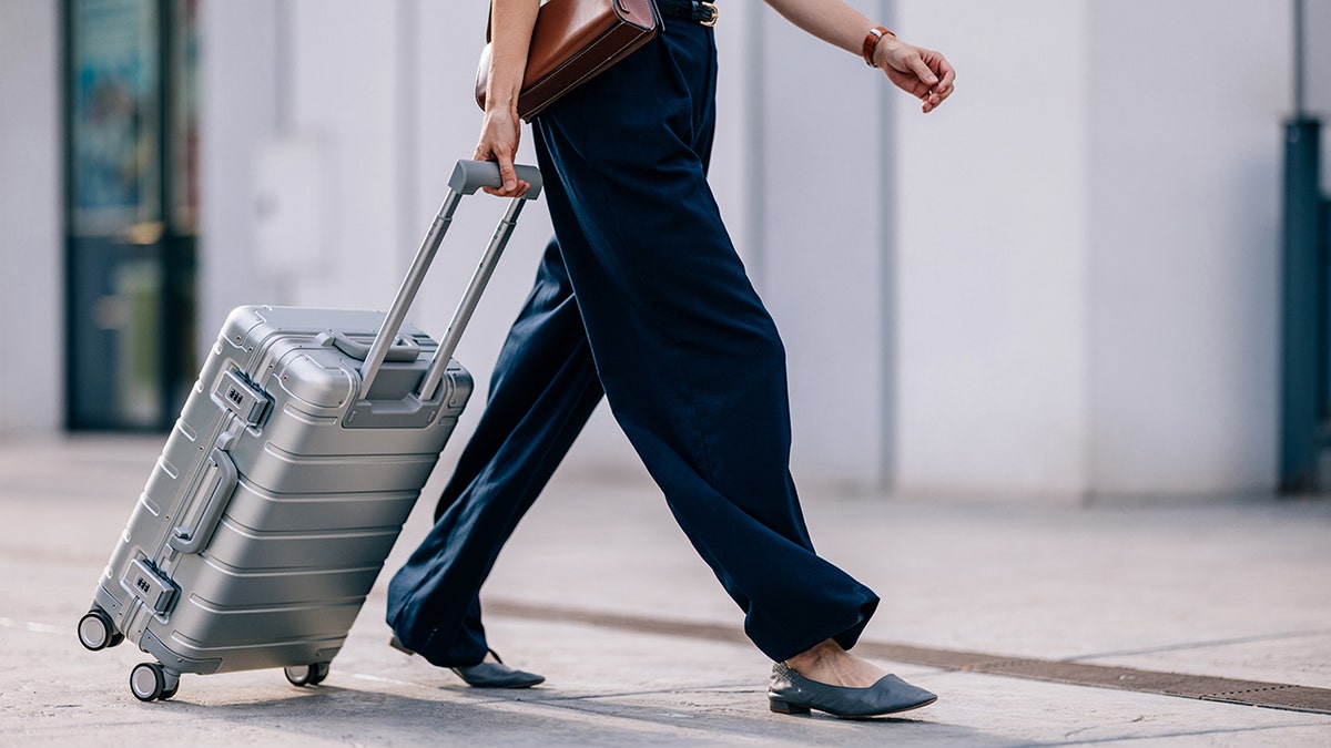 Close-up of a woman walking outside airport with a rolling suitcase.